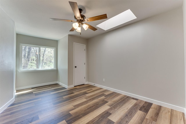 spare room with a skylight, wood finished floors, baseboards, and a ceiling fan
