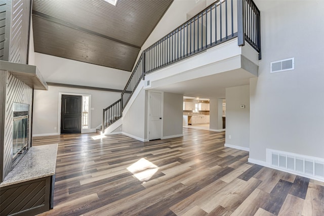 unfurnished living room with high vaulted ceiling, stairs, visible vents, and wood finished floors
