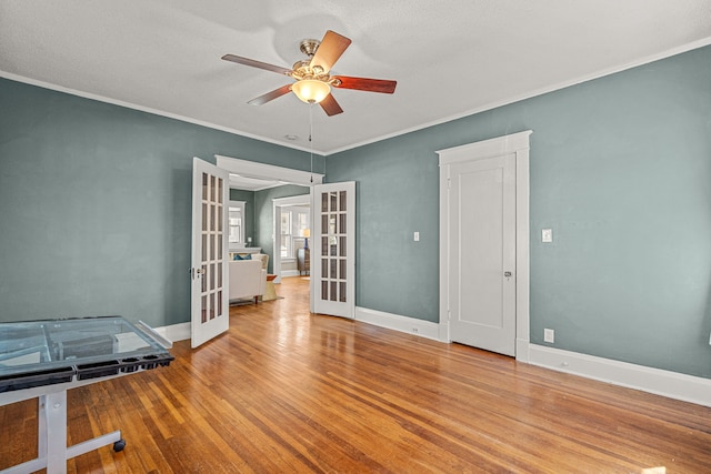 spare room with french doors, wood finished floors, baseboards, ceiling fan, and ornamental molding