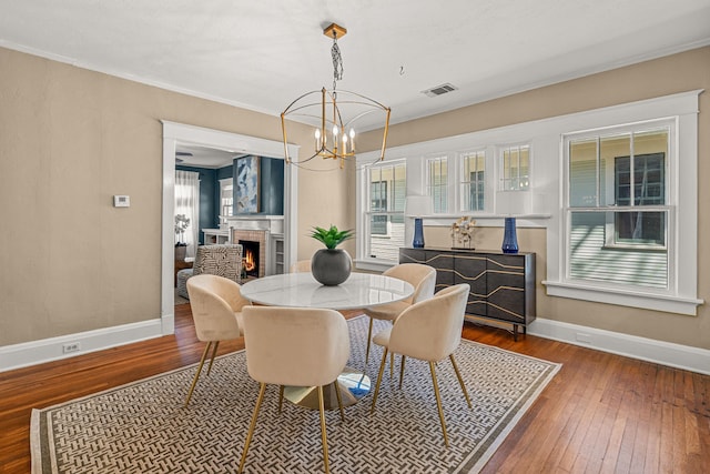 dining area featuring a warm lit fireplace, visible vents, baseboards, and wood-type flooring