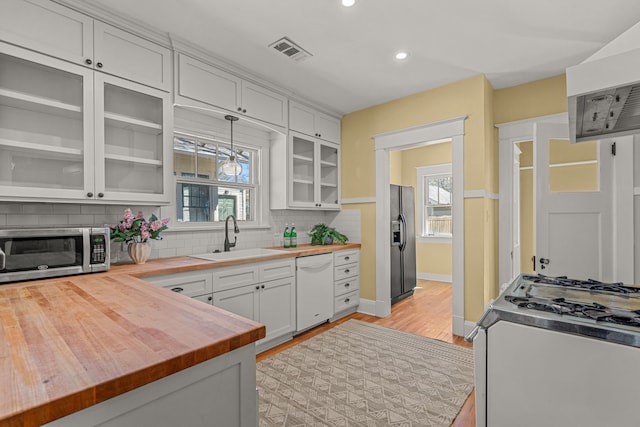 kitchen with black refrigerator with ice dispenser, stainless steel microwave, range with gas cooktop, wooden counters, and visible vents