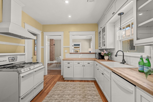 kitchen with custom exhaust hood, light wood finished floors, white appliances, glass insert cabinets, and a sink