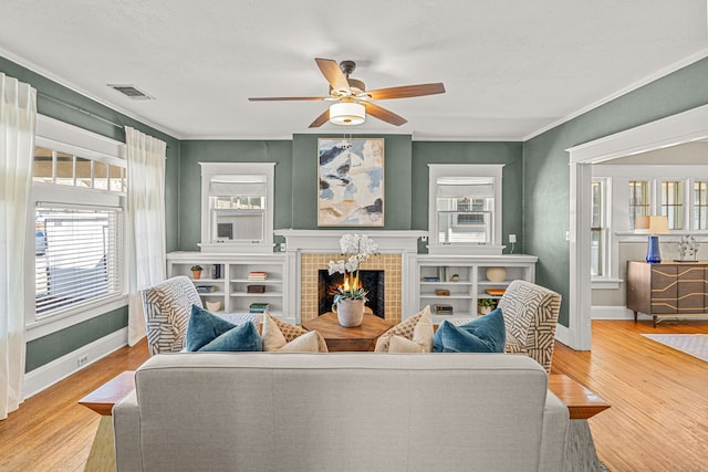 living room featuring a tile fireplace, wood finished floors, baseboards, visible vents, and ceiling fan