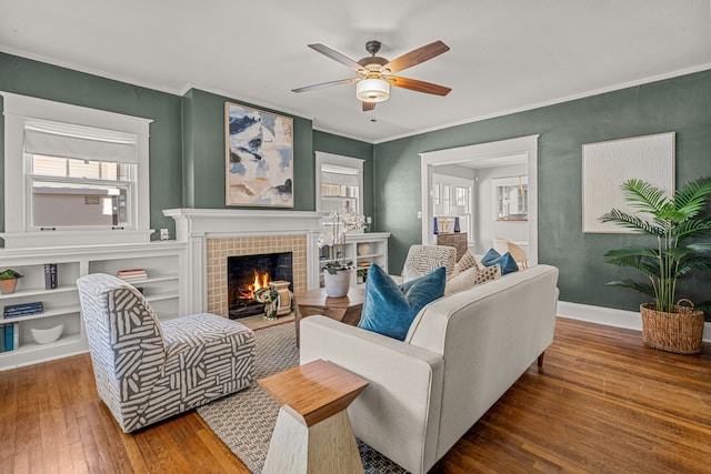 living area featuring crown molding, a ceiling fan, a fireplace, baseboards, and hardwood / wood-style floors
