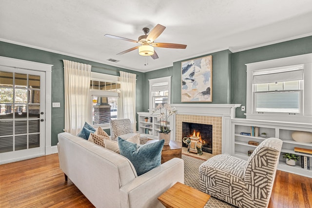 living area with ornamental molding, visible vents, a ceiling fan, a fireplace, and wood finished floors