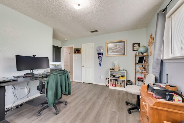 office space with visible vents, baseboards, light wood-type flooring, and a textured ceiling
