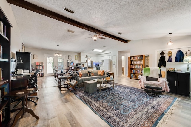 living area with visible vents, a textured ceiling, light wood finished floors, ceiling fan with notable chandelier, and vaulted ceiling with beams