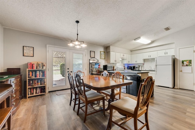 dining room with french doors, light wood finished floors, vaulted ceiling, and visible vents