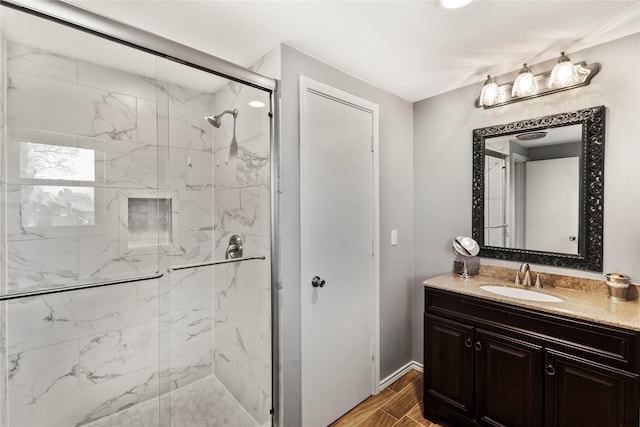 bathroom with baseboards, wood finished floors, vanity, and a stall shower