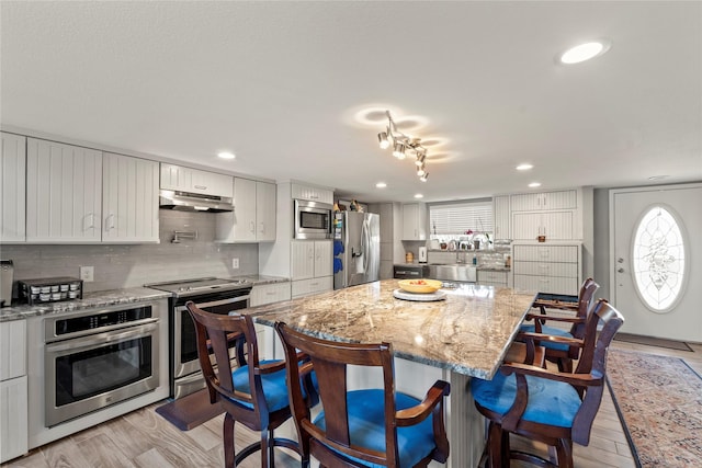 kitchen featuring stainless steel appliances, light wood-style flooring, under cabinet range hood, and a breakfast bar area