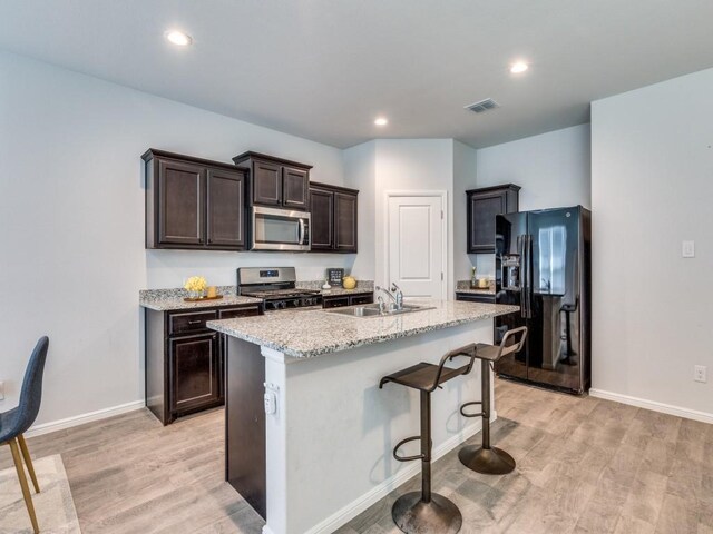 kitchen with visible vents, stainless steel appliances, dark brown cabinetry, a sink, and light wood-style floors