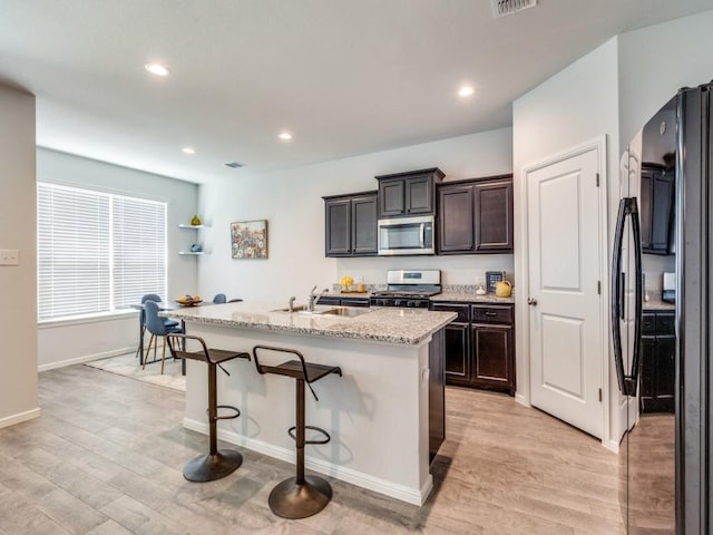 kitchen featuring a kitchen bar, a sink, stainless steel appliances, and light wood-type flooring
