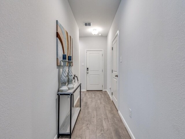 hall featuring light wood finished floors, baseboards, and visible vents