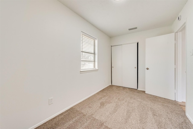 unfurnished bedroom with a closet, visible vents, light colored carpet, and baseboards