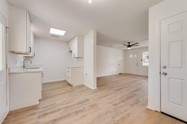 kitchen featuring a sink, ceiling fan, light wood-type flooring, light countertops, and white cabinets