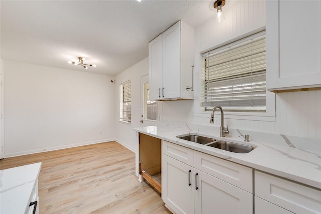 kitchen featuring light wood-style flooring, light stone countertops, a sink, and white cabinetry