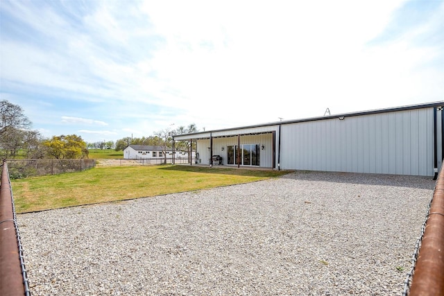 view of pole building with driveway, fence, and a lawn
