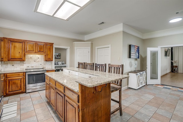 kitchen featuring decorative backsplash, stainless steel range with electric stovetop, brown cabinets, a center island, and a kitchen breakfast bar