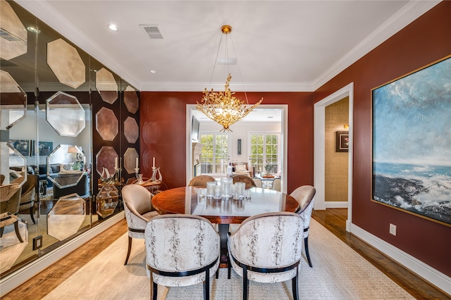 dining space featuring visible vents, baseboards, a notable chandelier, crown molding, and wood finished floors