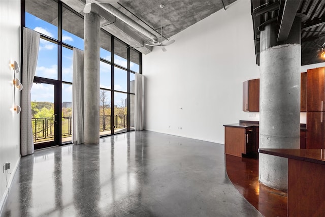 unfurnished living room with concrete floors, a towering ceiling, and decorative columns