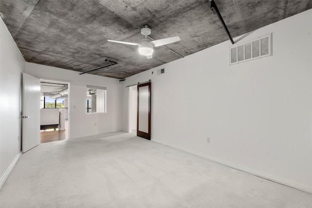 unfurnished room featuring visible vents, a barn door, carpet, and a ceiling fan