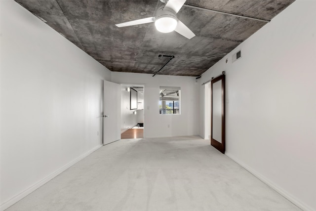 carpeted spare room featuring a ceiling fan, baseboards, visible vents, and a barn door