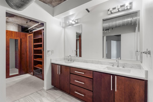 bathroom with double vanity, a walk in closet, and a sink
