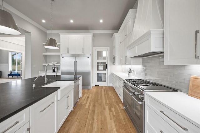 909 Saint Anne Ct, Heath, TX 75032 - kitchen with premium range hood, premium appliances, a sink, light wood-style floors, and white cabinetry