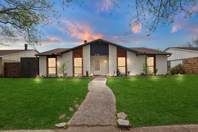 mid-century modern home with a gate, brick siding, and a yard