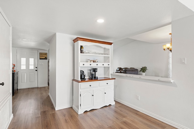 hallway with baseboards, visible vents, an inviting chandelier, and light wood-type flooring