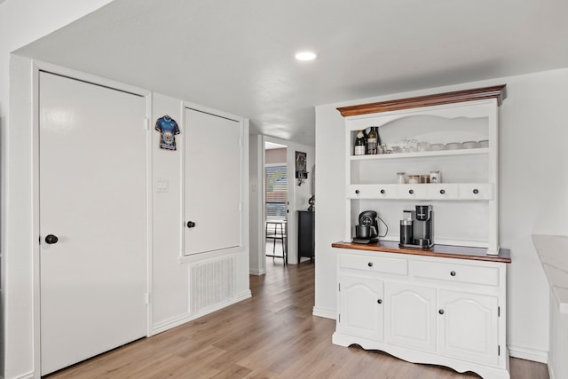 bar featuring light wood finished floors, baseboards, and visible vents
