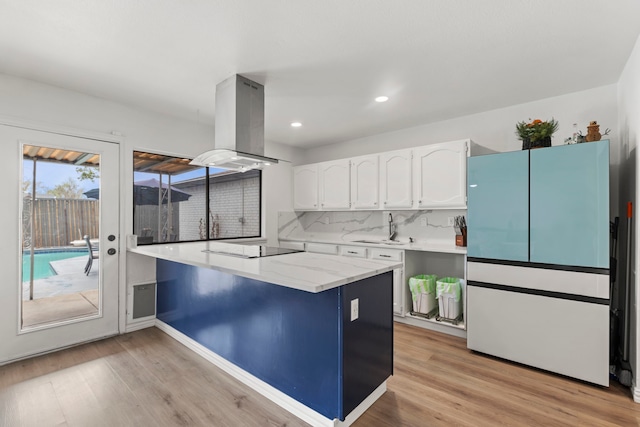 kitchen featuring white cabinets, light wood-style flooring, a sink, island range hood, and backsplash