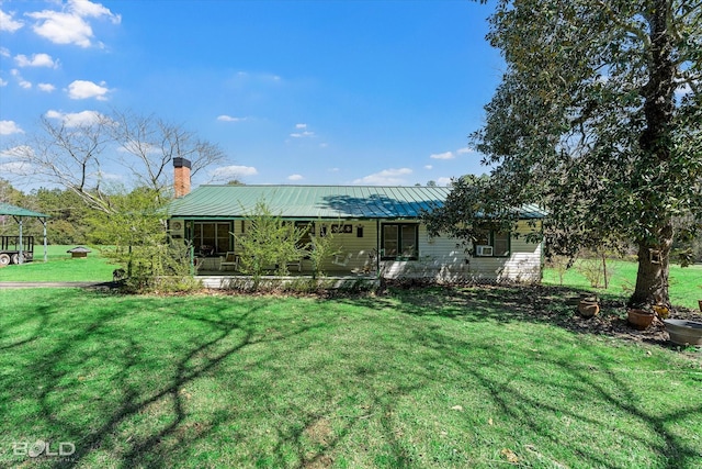 back of house featuring metal roof, a chimney, and a yard