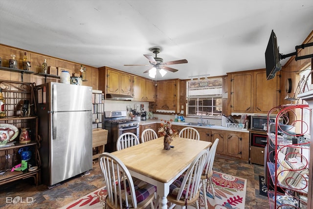 kitchen featuring brown cabinets, stainless steel appliances, under cabinet range hood, and stone finish floor
