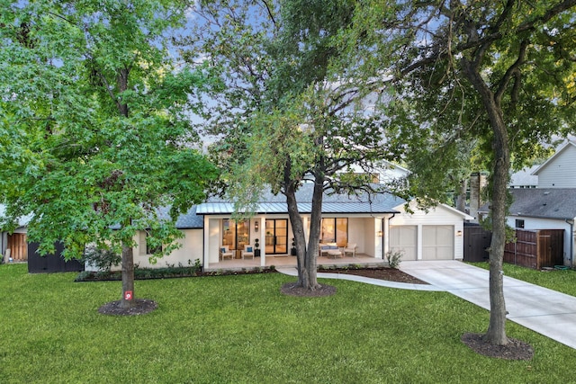 view of front facade featuring a front yard, a standing seam roof, concrete driveway, fence, and an attached garage