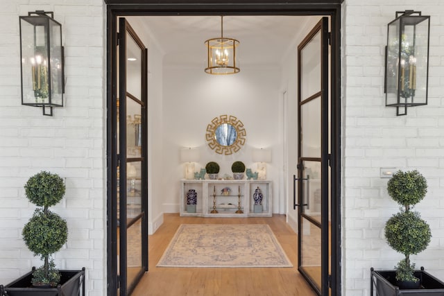 interior space featuring brick wall, crown molding, light wood-style floors, and a chandelier