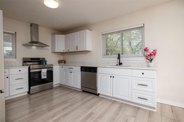 kitchen with light wood finished floors, a sink, wall chimney range hood, light countertops, and appliances with stainless steel finishes