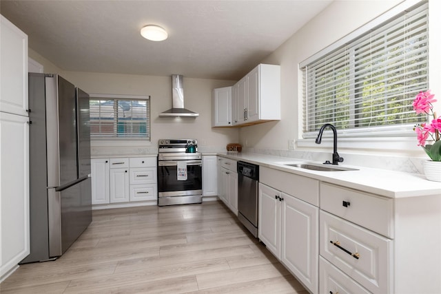 kitchen featuring wall chimney range hood, white cabinetry, stainless steel appliances, and a sink
