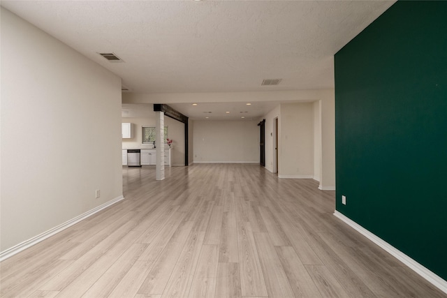 unfurnished living room with a textured ceiling, light wood-style floors, visible vents, and baseboards