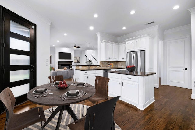 4929 Alcott St, Dallas, TX 75206 - dining room with dark wood-style floors, a warm lit fireplace, a ceiling fan, recessed lighting, and ornamental molding
