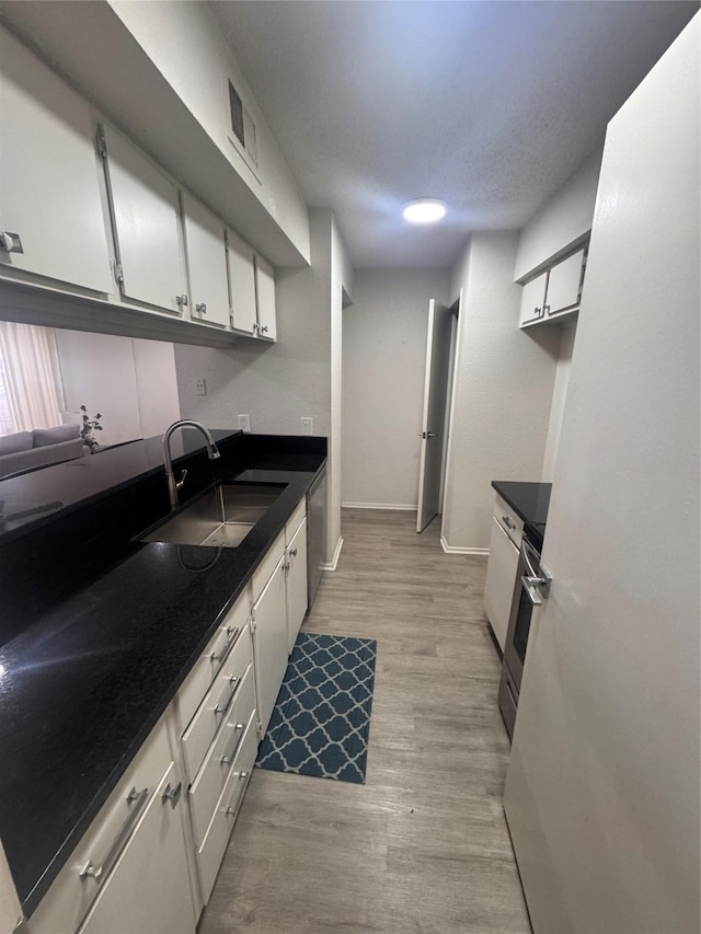kitchen featuring a sink, white cabinetry, light wood-type flooring, dark countertops, and stainless steel range oven