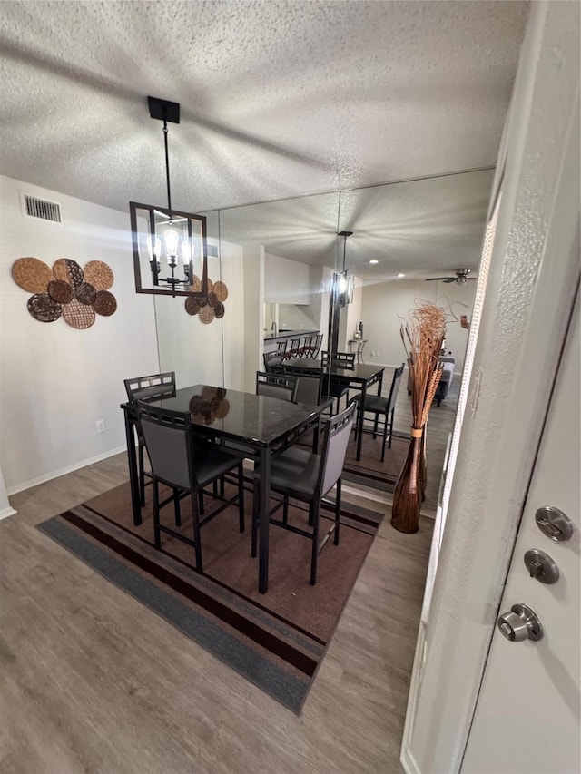 dining area featuring a chandelier, wood finished floors, a textured ceiling, baseboards, and visible vents