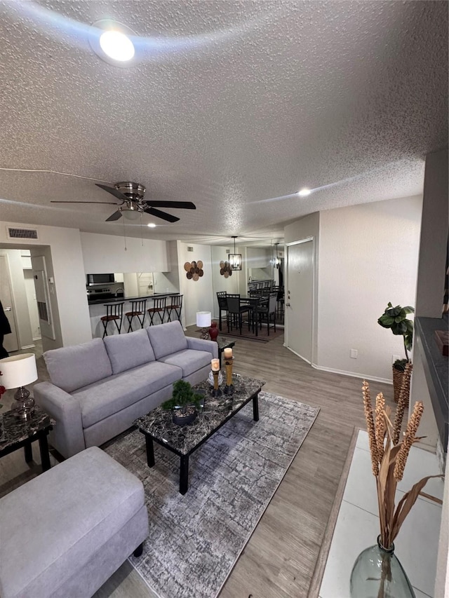 living room featuring a textured ceiling, visible vents, baseboards, wood finished floors, and a ceiling fan
