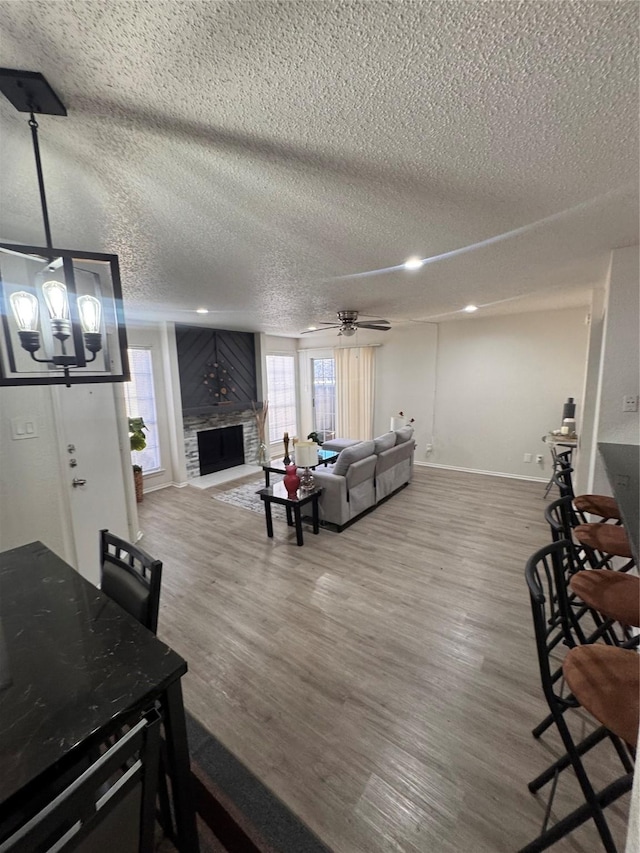 living room with a textured ceiling, baseboards, a fireplace, wood finished floors, and ceiling fan with notable chandelier