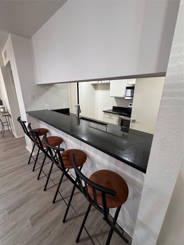 kitchen featuring white cabinetry, stainless steel appliances, a textured ceiling, a peninsula, and wood finished floors