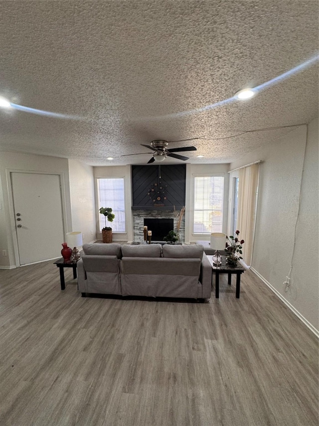 living room featuring baseboards, a textured ceiling, ceiling fan, a fireplace, and wood finished floors
