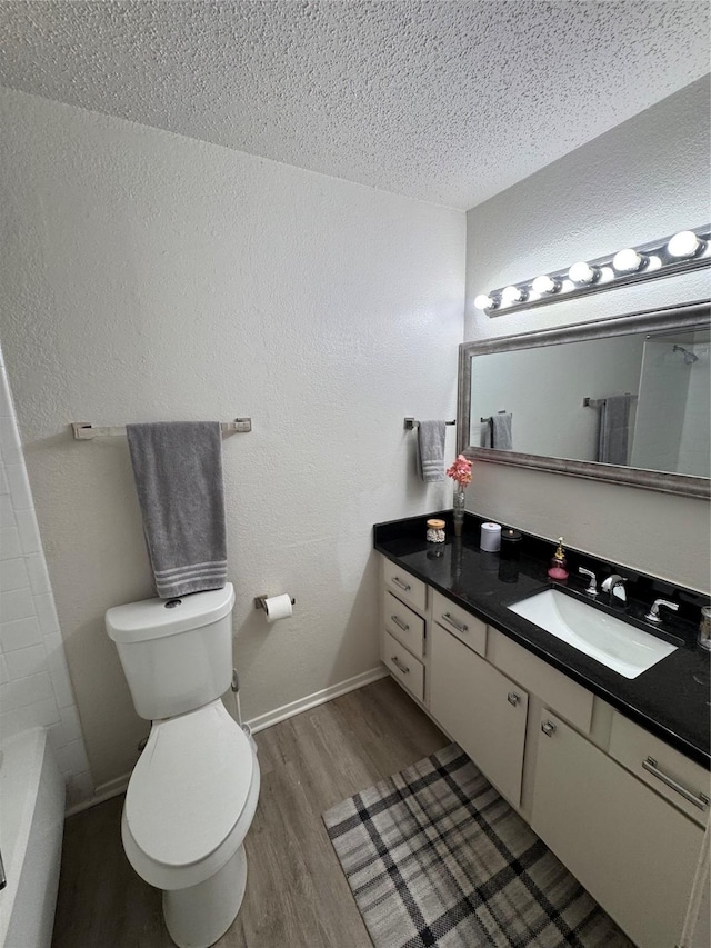 bathroom with a textured ceiling, wood finished floors, toilet, vanity, and a textured wall