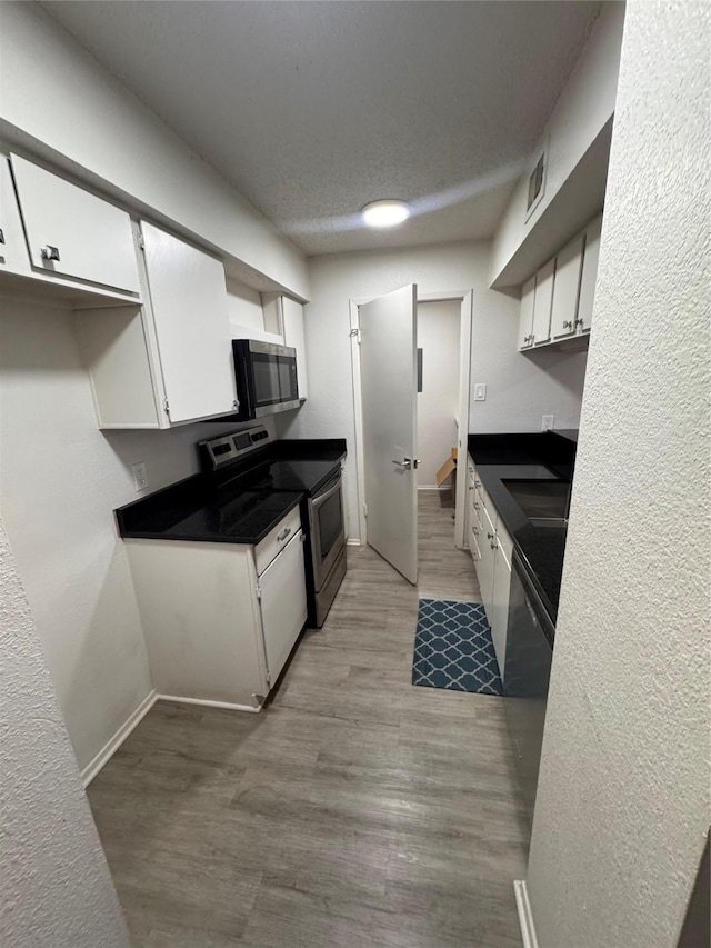 kitchen with white cabinets, dark countertops, appliances with stainless steel finishes, and wood finished floors