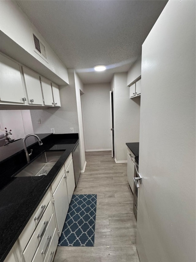 kitchen with a sink, dark countertops, light wood finished floors, visible vents, and white cabinets