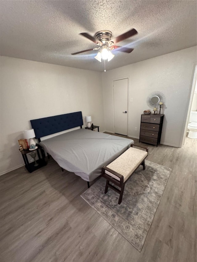 bedroom featuring a textured ceiling, light wood-style flooring, baseboards, a ceiling fan, and ensuite bath